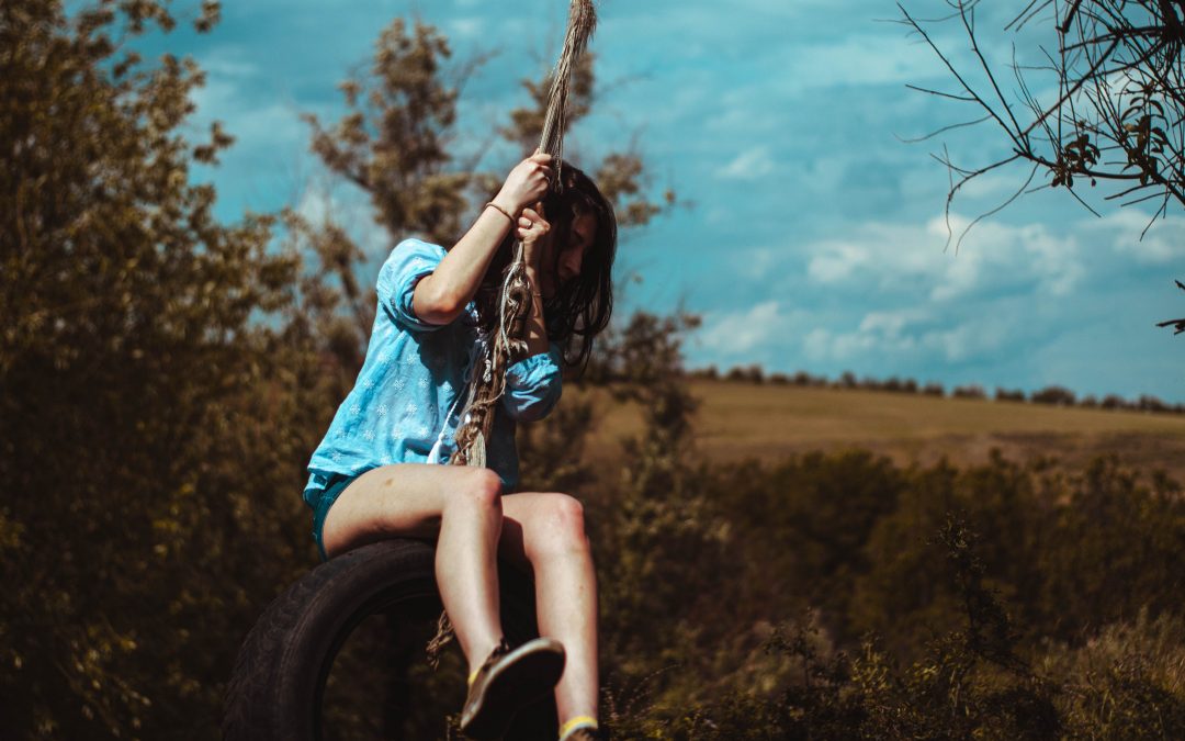 woman in blue and white plaid shirt sitting on tire swing during daytime