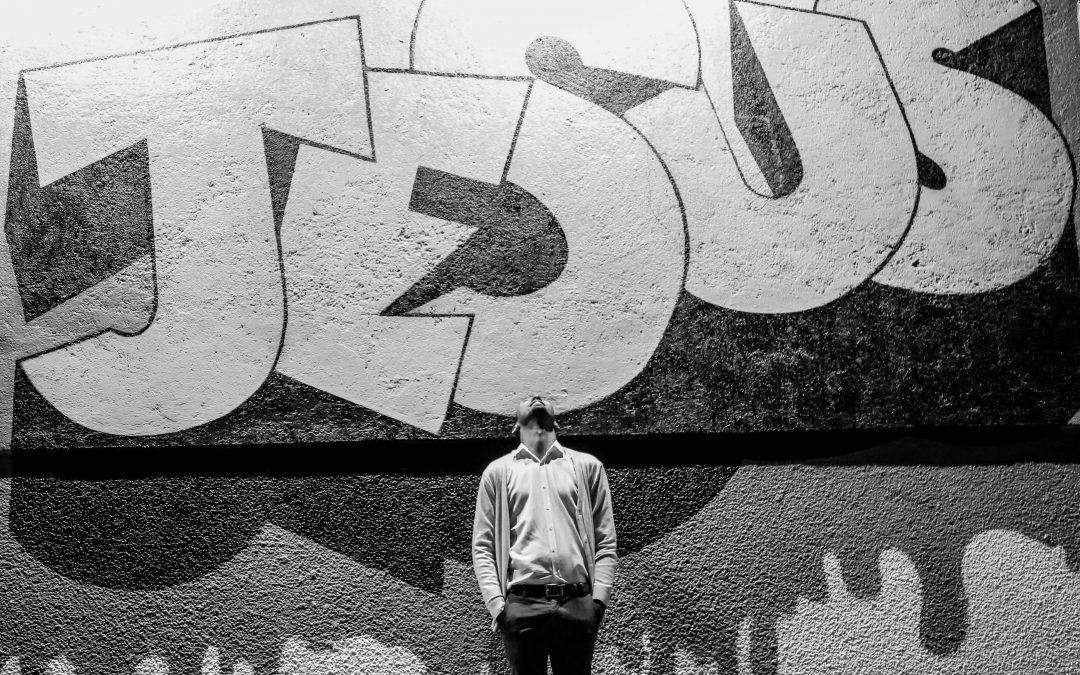 grayscale photography of a man standing in front of a Jesus graffiti