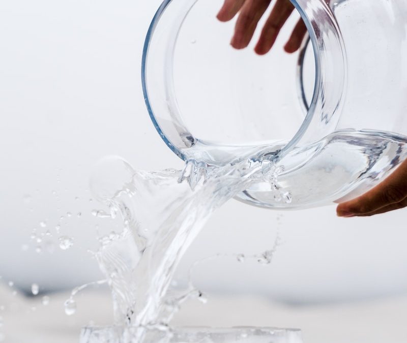 person holding clear glass jar with water