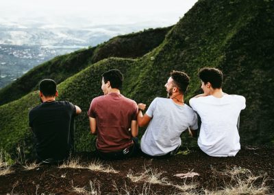 row of four men sitting on mountain trail