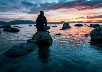 man sitting on rock surrounded by water