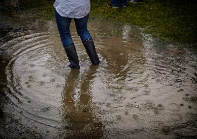 person with rain boots standing on body of water