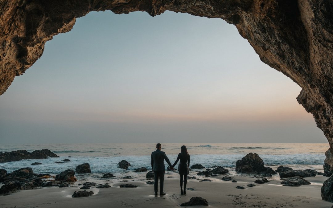 man and woman holding hands facing sea