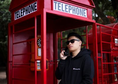 man in black sunglasses and black hoodie standing near red telephone booth