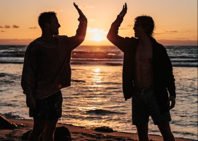 silhouette of two mens near seashore about to high five during sunset