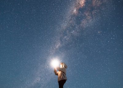 man in white shirt and black shorts standing on rock under starry night