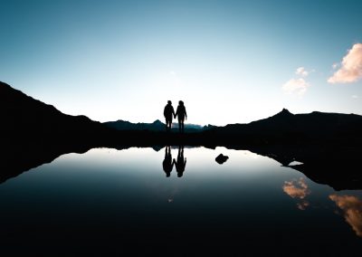 silhouette of people holding hands in front of body of water under blue sky