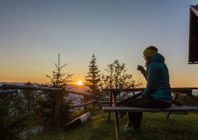 woman in blue bubble jacket sitting and having a coffee on mountain during sunrise
