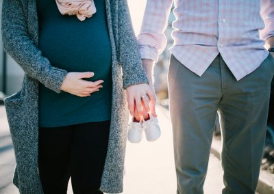 man standing beside pregnant woman holding baby's shoes during daytime