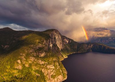 body of water near mountain with rainbow during daytime